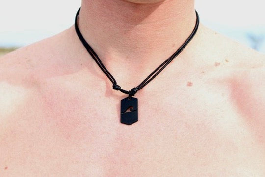 Black dog tag necklace with cut-out wave pendant laid flat